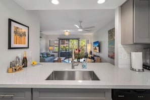 A modern kitchen with a stainless steel sink, a ceiling fan, and a dining area with a view of the outdoors.
