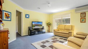 A living room with a television, a beige sofa, a coffee table, and a patterned rug. - Alkira Inverloch Holiday (Inverloch)
