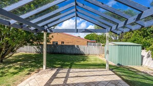 A covered patio area with a view of a brick house and a green shed. - Alkira Inverloch Holiday (Inverloch)