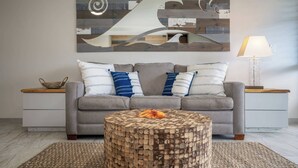 Ein modernes Wohnzimmer mit grauem Sofa, rundem Holztisch und abstrakter Wandkunst.