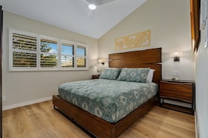 A bedroom with a bed, a window with blinds, a nightstand, and a wall-mounted light.