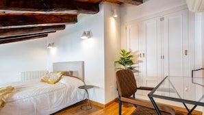 Un dormitorio con cama, mesita de noche, silla y una planta en maceta.