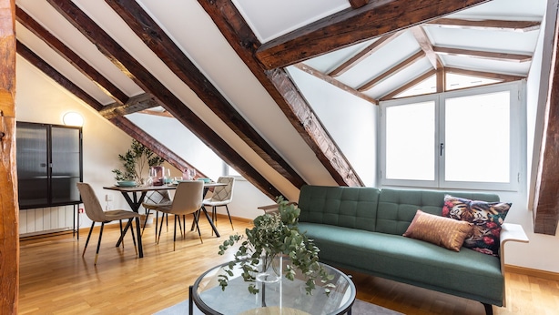Un acogedor espacio tipo loft con vigas de madera a la vista, un sofá verde, una mesa de centro de vidrio y un área de comedor con una mesa y sillas.