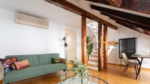 Una sala de estar con un sofá verde, una mesa de centro de vidrio, piso de madera, una escalera y un comedor con mesa y sillas.