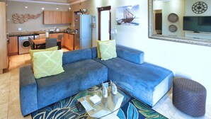 A living room with a blue sofa, a glass coffee table, and a patterned rug.