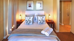 A neatly made bed with a striped blanket, two bedside lamps, and a pair of pillows with a floral design.