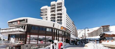 A ski resort building with multiple floors, a ski lift, and a snowy landscape.