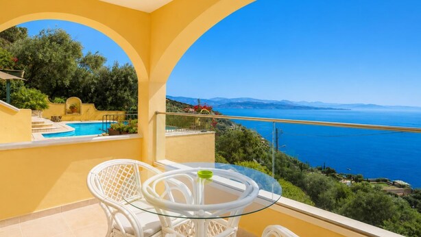 Un balcon avec une table et des chaises en verre, donnant sur une piscine et offrant une vue panoramique sur la mer.