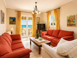 Una sala de estar con un sofá, una mesa de centro, un televisor y vistas al mar a través de un ventanal.