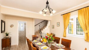 Un coin repas avec une table en bois dressée pour quatre personnes, un escalier en arrière-plan et une plante en pot sur la gauche.