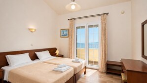 Une chambre d’hôtel avec deux lits, un balcon avec des rideaux, une lampe fixée au mur et un petit tableau.
