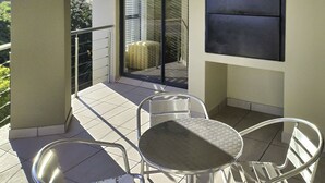 Un balcon avec une table et des chaises, une porte-fenêtre donnant sur l’extérieur et un téléviseur fixé au mur.