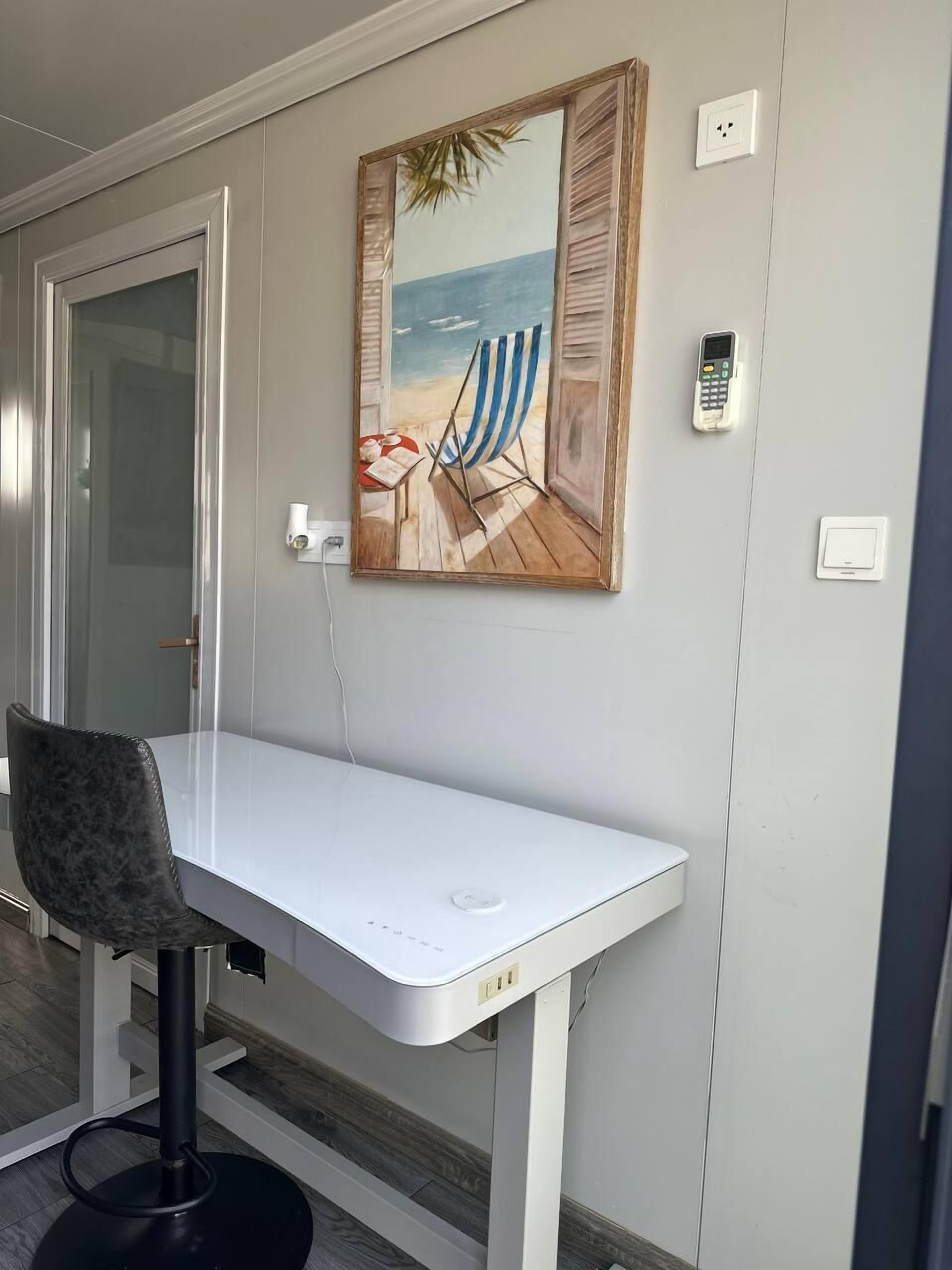 A modern room with a white desk, a chair, and a beach-themed painting.