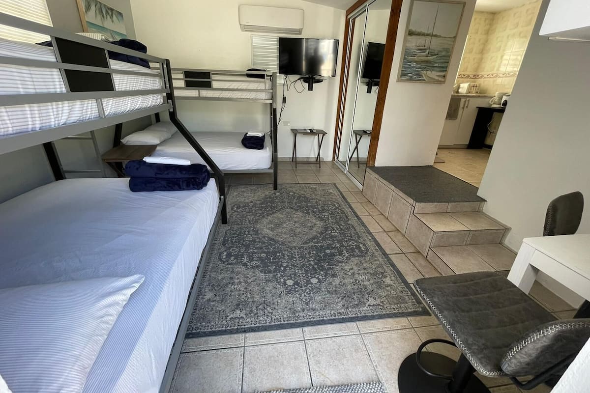 Ein kleines Hotelzimmer mit Etagenbetten, einem kleinen Schreibtisch, einem Fernseher und einem durch eine Glastür einsehbarer Badezimmer.