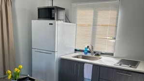 A compact kitchen with a refrigerator, a microwave, a sink, and a window with blinds. - Las Casitas de Village (Carolina)