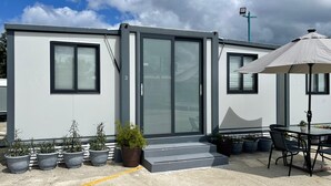 A modern building with a glass door entrance, potted plants, and a patio area with a table and chairs. - Las Casitas de Village (Carolina)