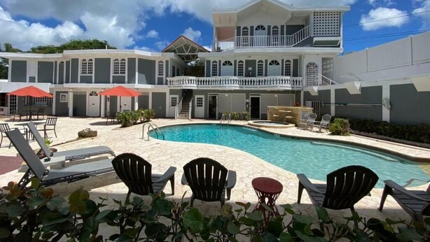 A hotel with a swimming pool, outdoor seating, and a two-story building with balconies. - Las Casitas de Village (Carolina)