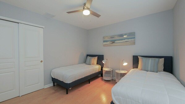 A bedroom with two single beds, a ceiling fan, a painting on the wall, and a white door.