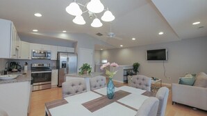 Una cocina moderna con electrodomésticos integrados, un comedor con mesa y sillas, y una sala de estar con sofá y televisor.