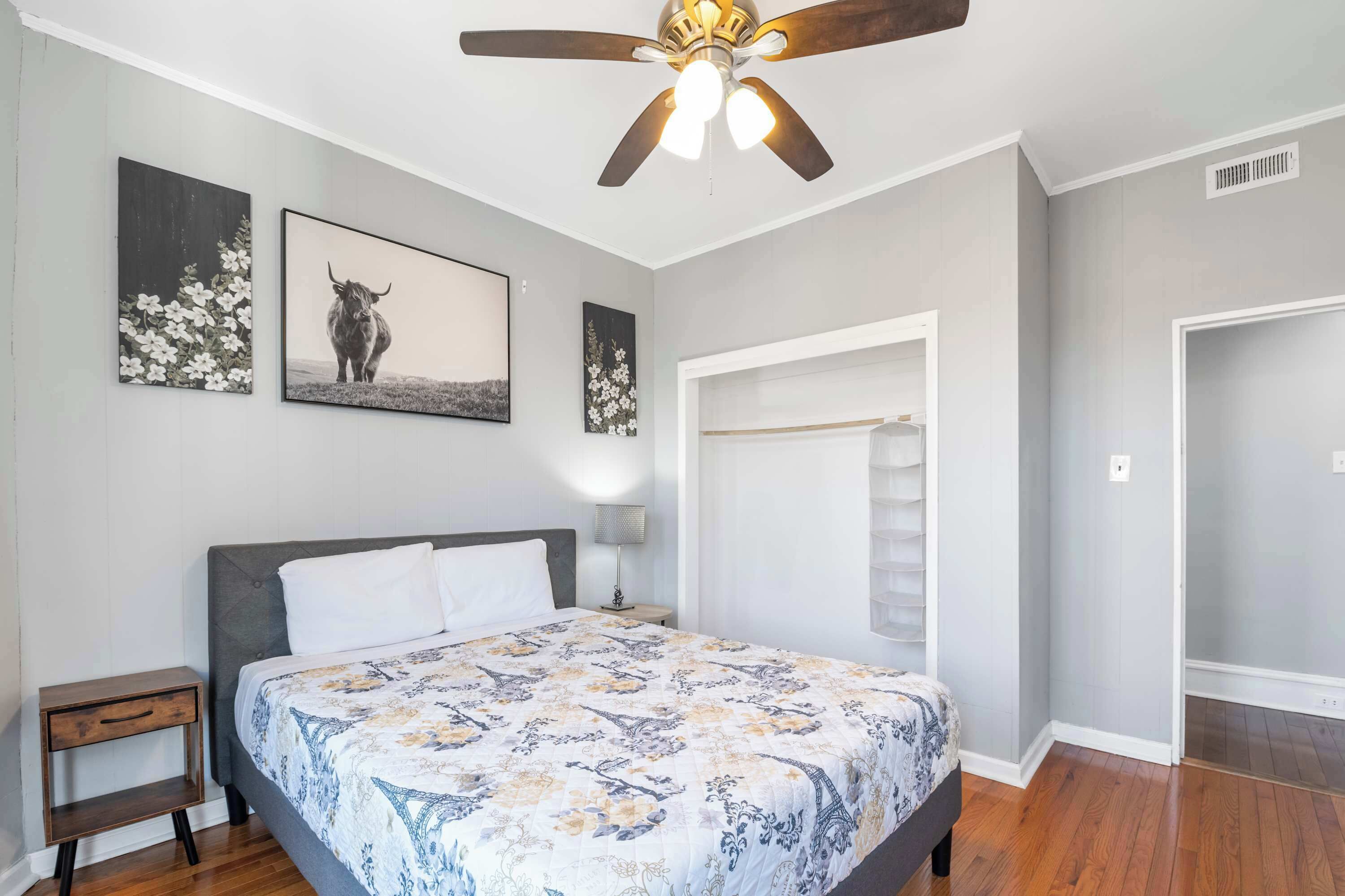 A bedroom with a bed, a ceiling fan, and artwork on the walls.