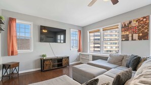 A modern living room with a large sectional sofa, a flat-screen TV mounted on the wall, and a ceiling fan. - Rustic Paradise - Steps to Beach! (Atlantic City)