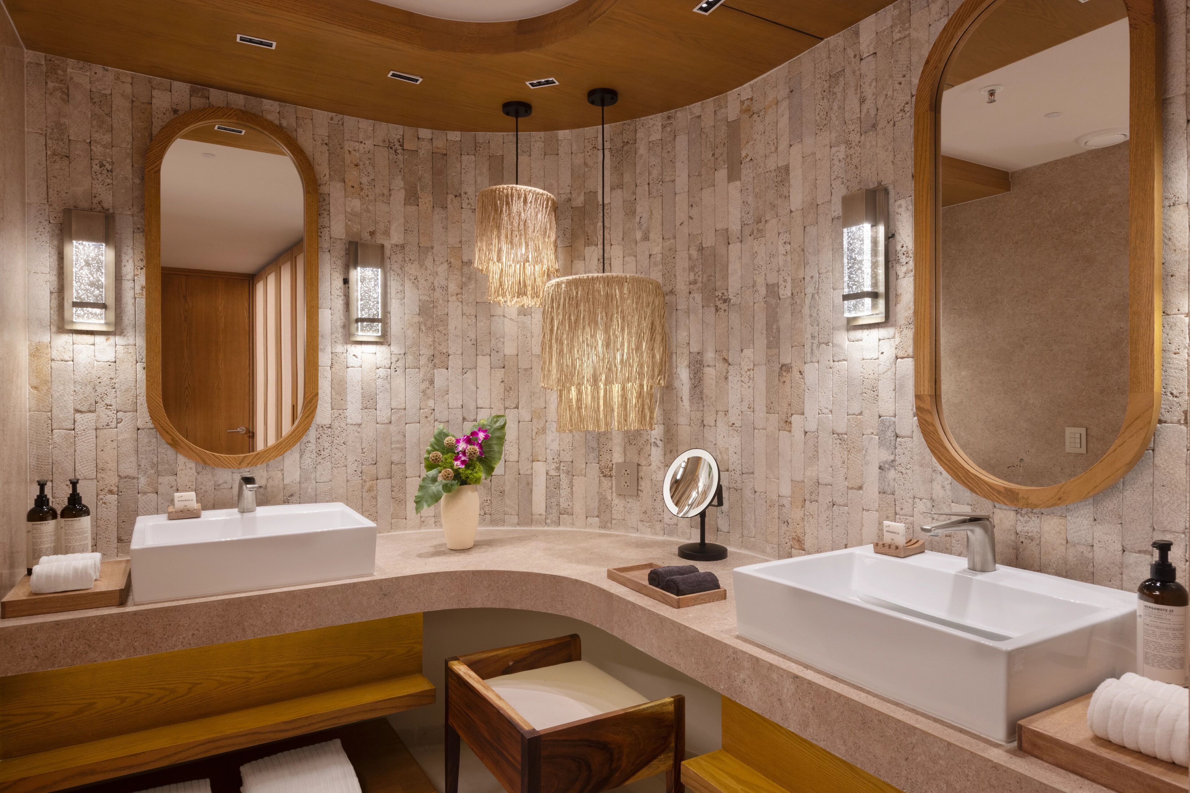A modern bathroom with two sinks, wooden benches, and a large mirror.