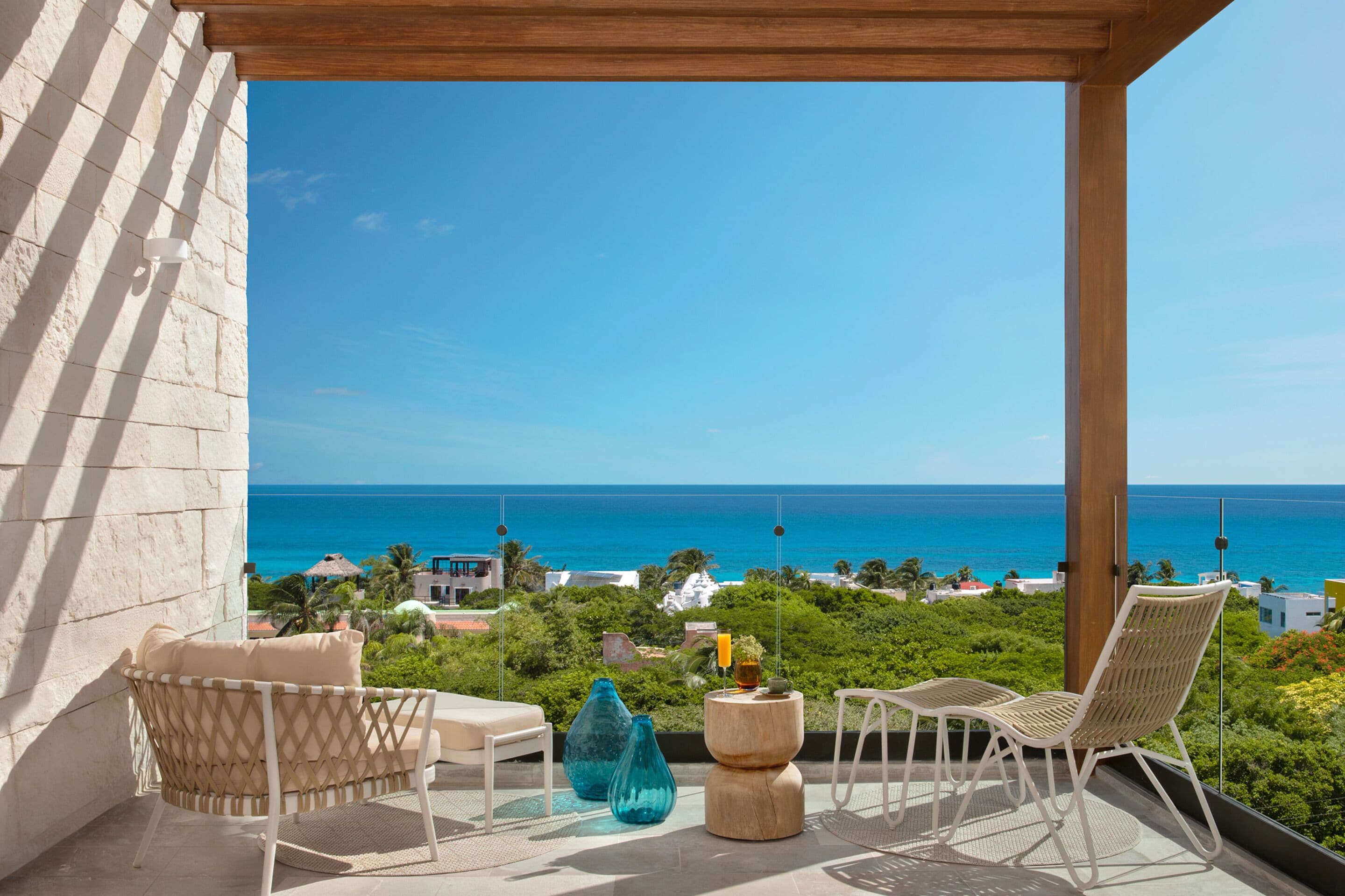 A balcony with wicker chairs, a small table, and a view of the ocean.