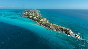 An aerial view of a coastal island with clear turquoise waters, a narrow strip of land with buildings, and a rugged coastline.