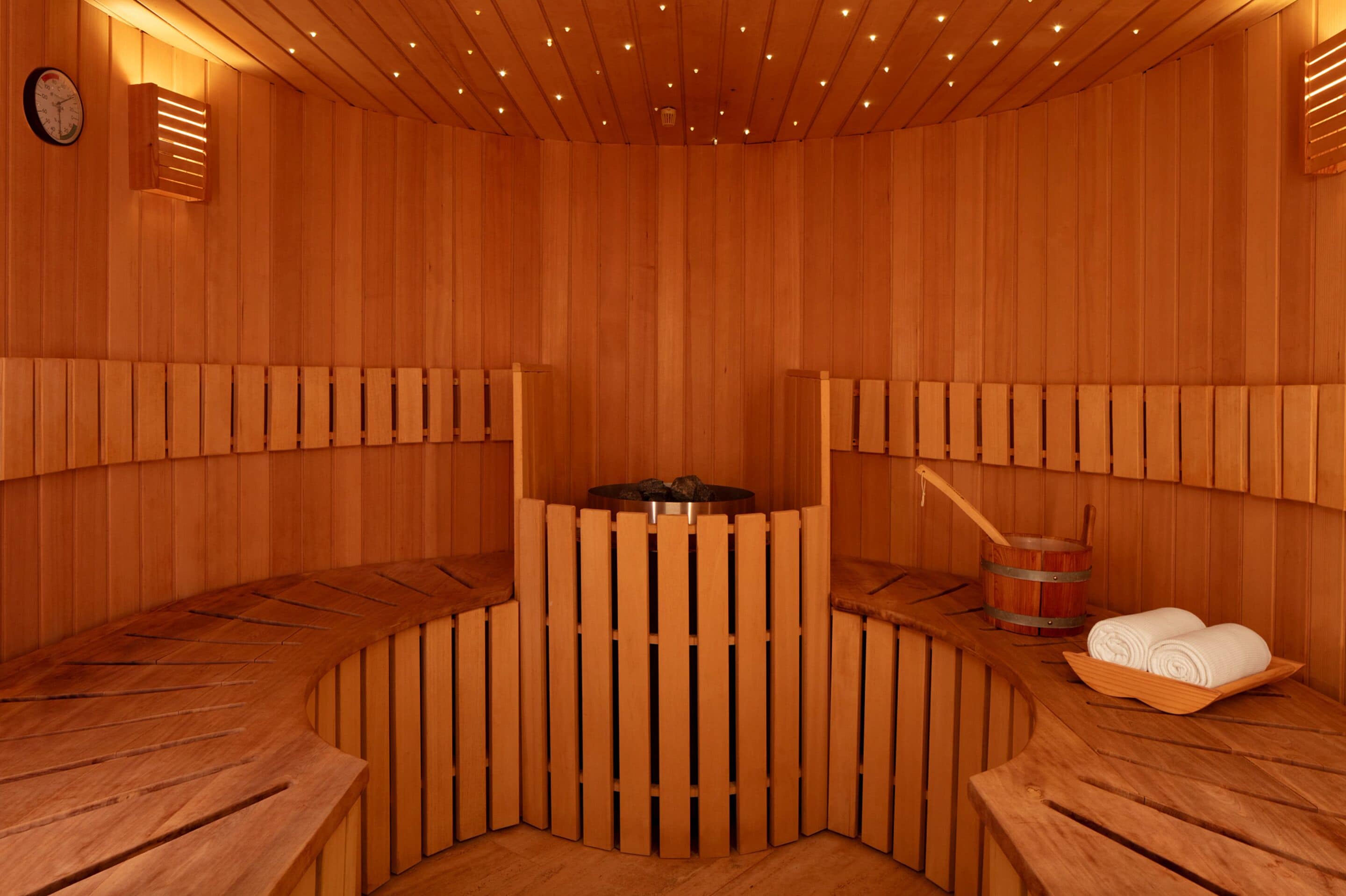 A wooden sauna with benches, a central heating element, and a bucket.