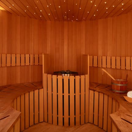 A wooden sauna with benches, a central heating element, and a bucket.