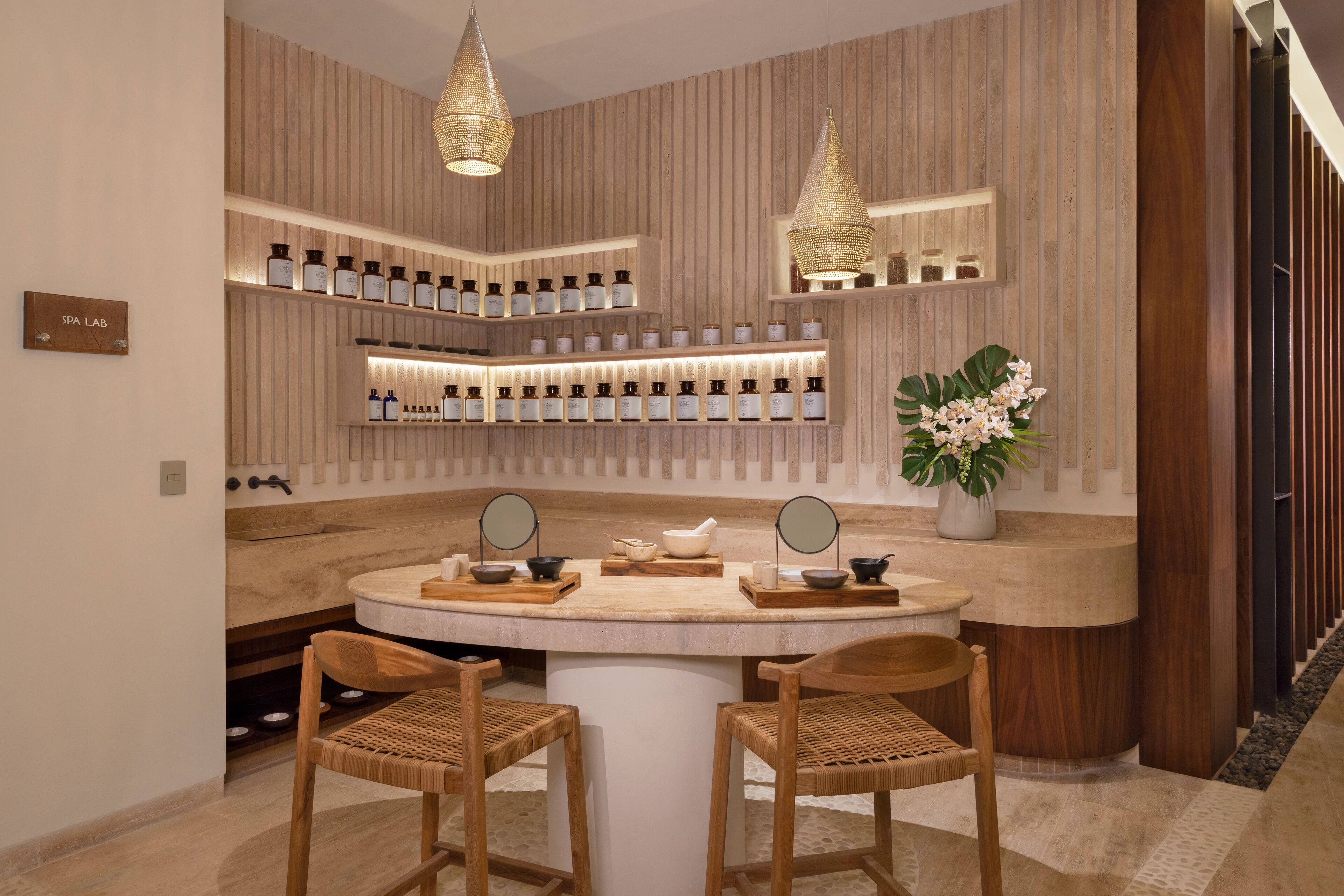 A spa lab with wooden panel walls, shelves with bottles, a round table with chairs, and two hanging lamps.