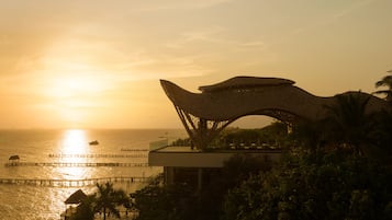 A modern architectural structure with a unique roof design, overlooking a body of water with a pier extending into the sea.