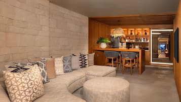 A modern living area with a curved sofa, a round ottoman, and a wooden bar with a hanging lamp.