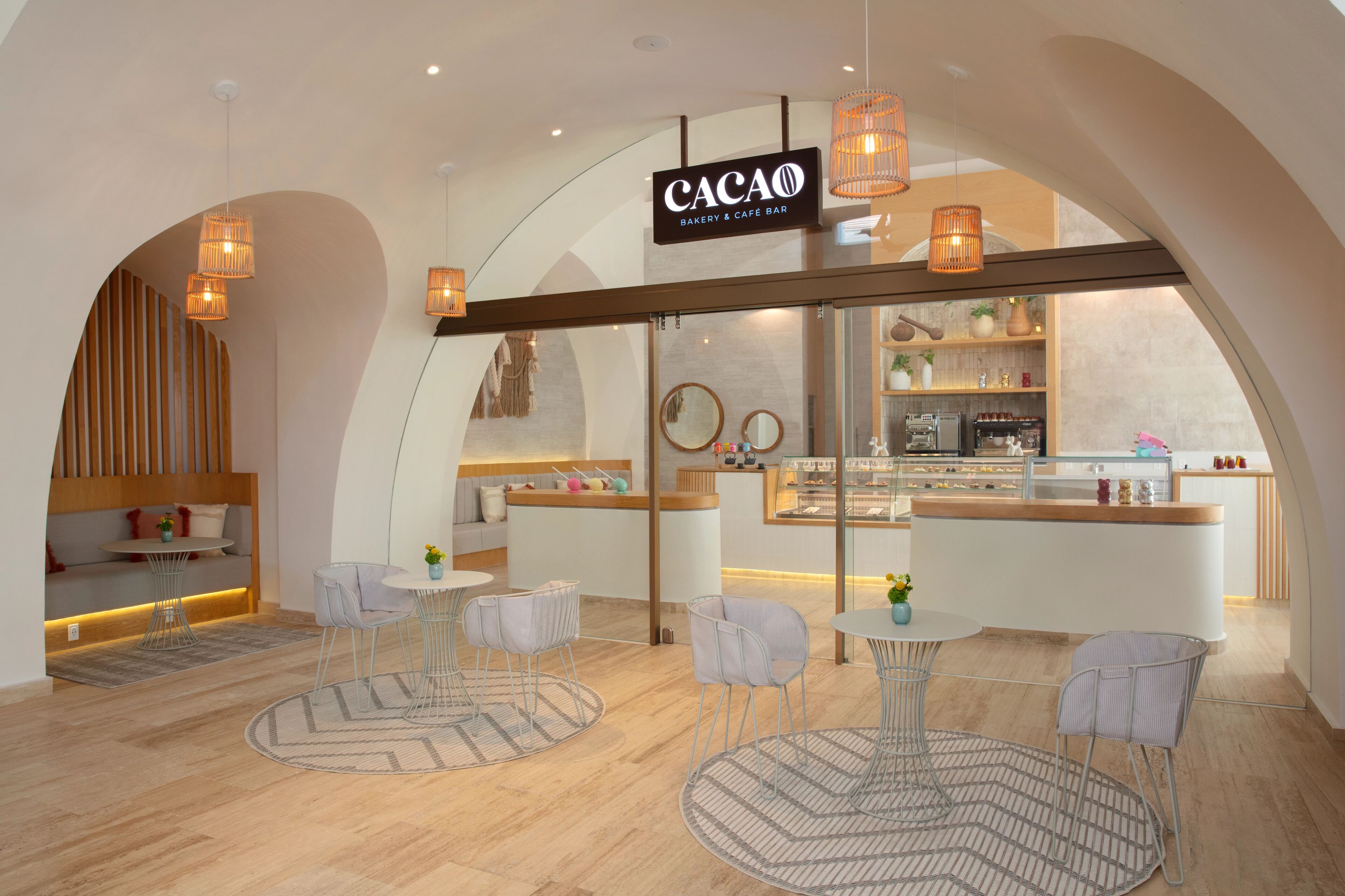A modern interior with a bakery and cafe bar named Cacao, featuring round tables, chairs, and a visible kitchen area.