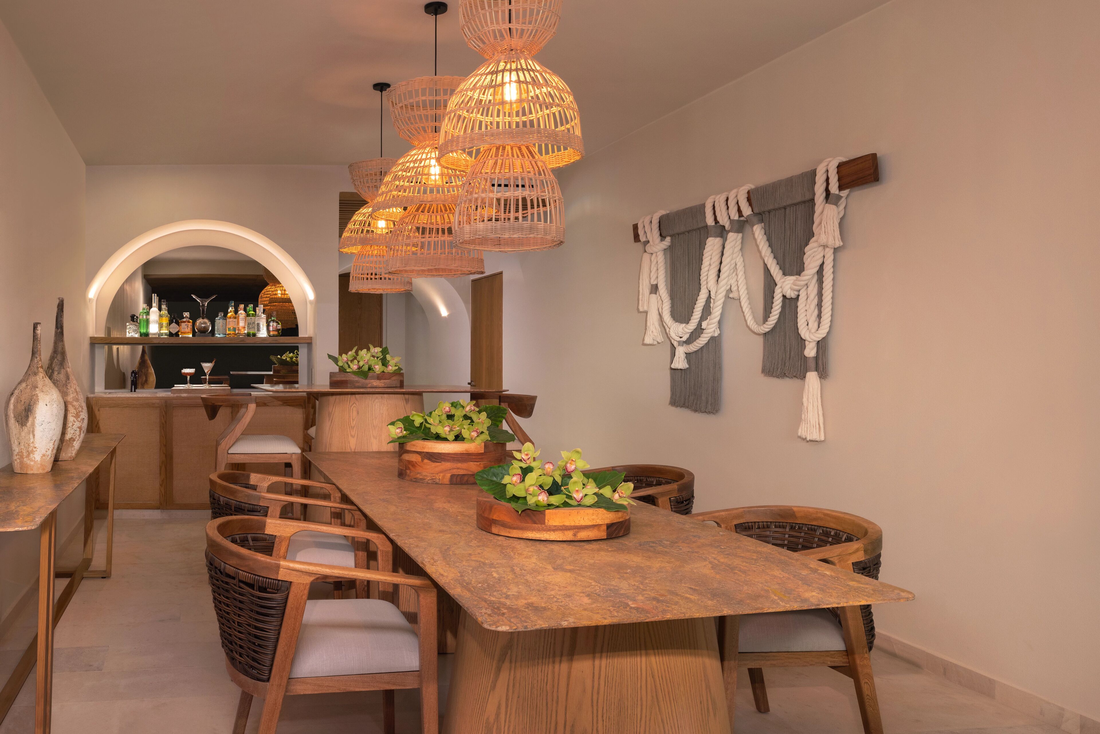 A dining area with a long wooden table, wicker chairs, and hanging wicker light fixtures.