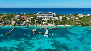 Eine Vogelperspektive zeigt einen Küstenort mit einer Marina, klarem türkisblauem Wasser und einem großen Hotelgebäude.