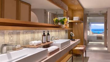 Une salle de bain moderne avec deux vasques, des étagères en bois, un miroir et une vue sur la mer.