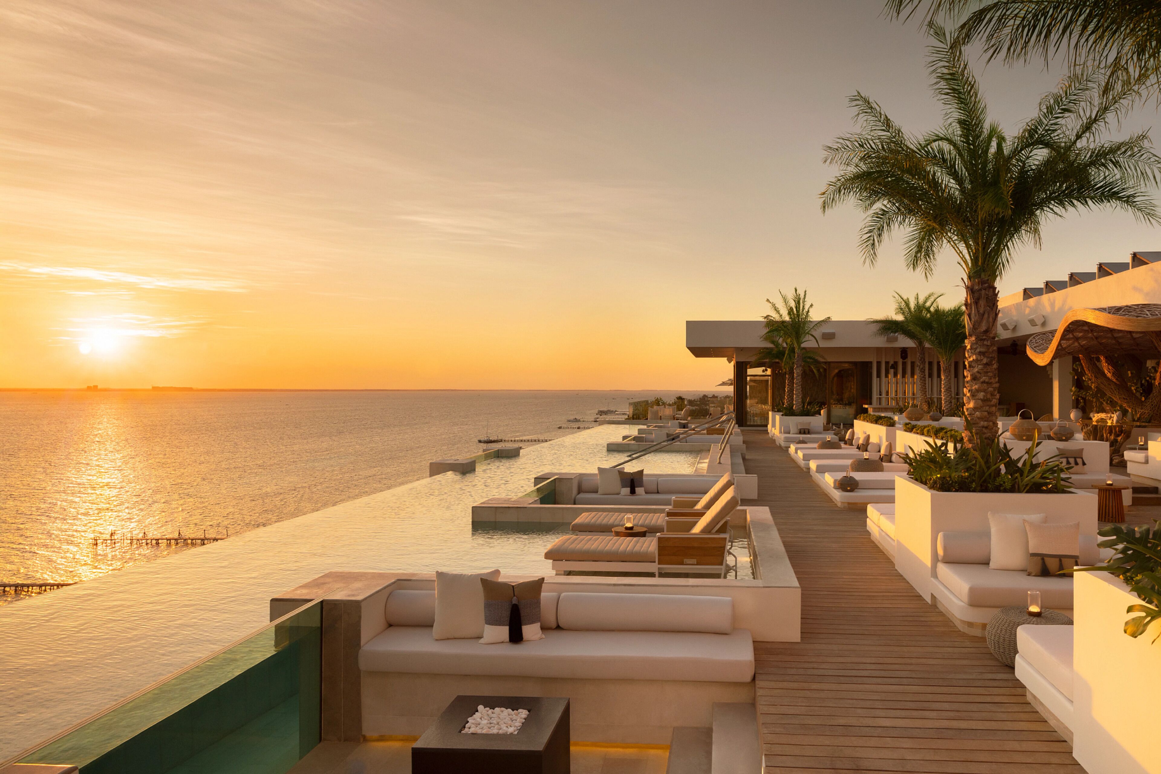 A sunlit outdoor lounge area with seating and a view of the sea at sunset.