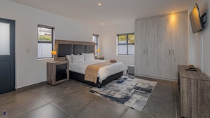 Quarto moderno com cama grande, roupeiro embutido e televisão na parede.