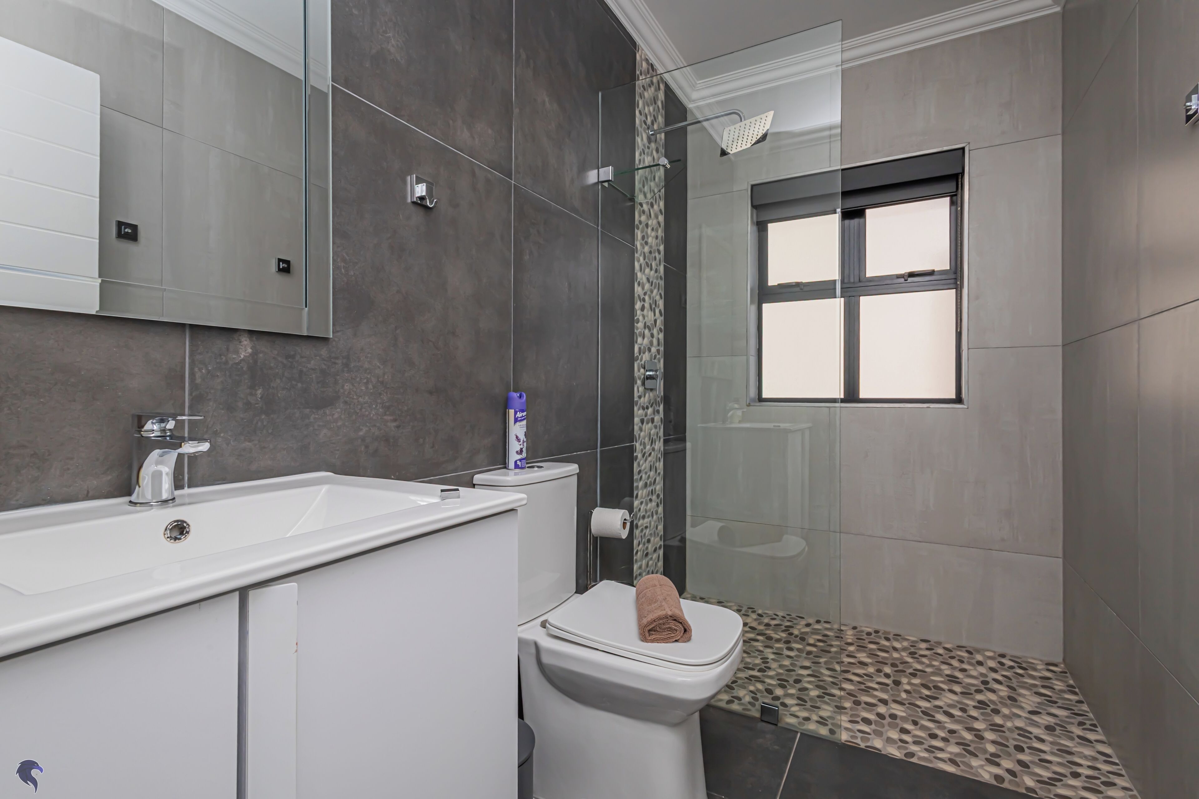 Un baño moderno con un espejo grande, un lavabo blanco, un inodoro y una zona de ducha.