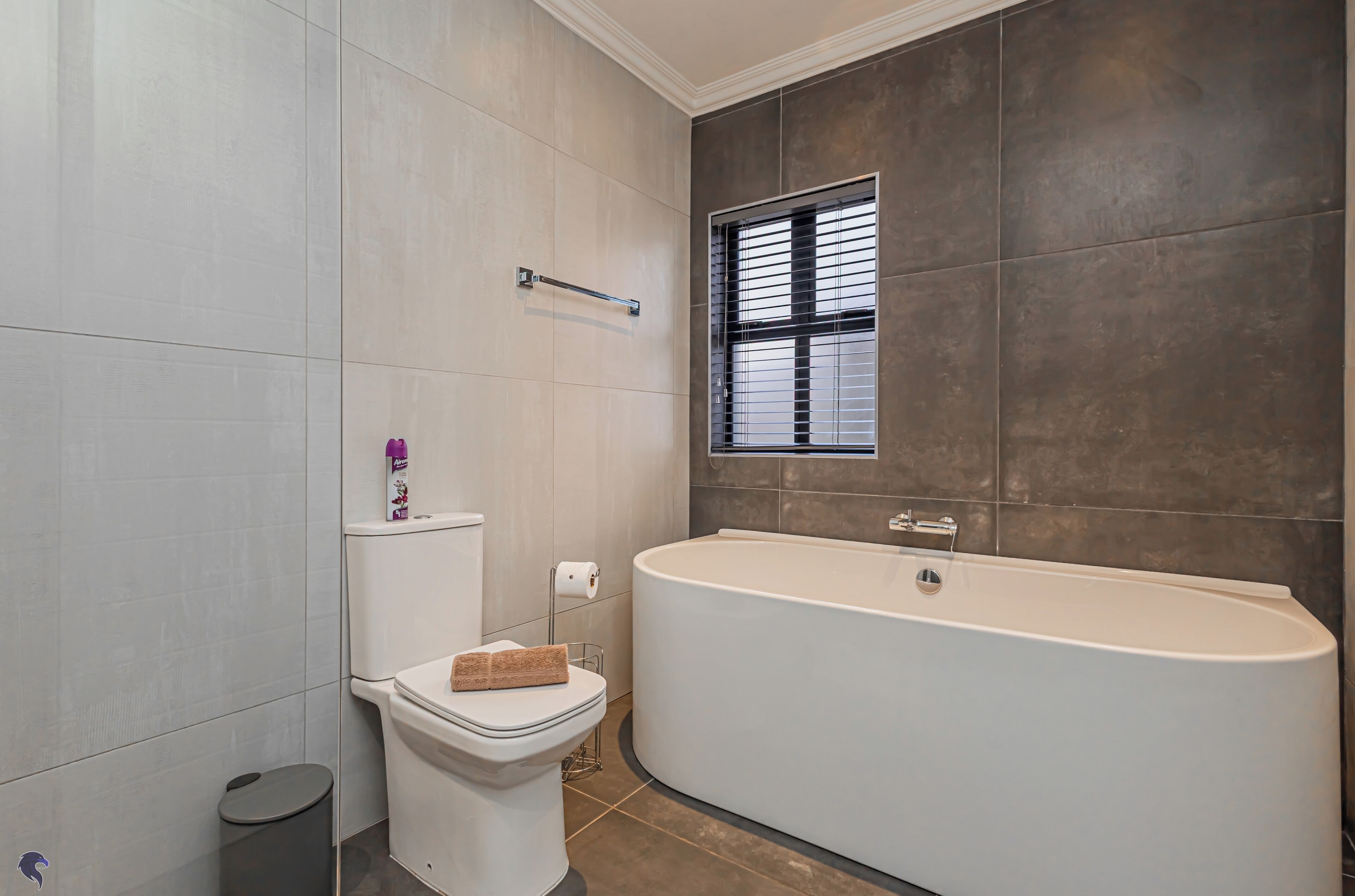 A modern bathroom with a bathtub, toilet, and window.