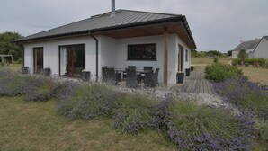 Una casa moderna con un porche cubierto, un comedor y un jardín con plantas de lavanda.