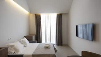 Habitación de hotel con cama, mesita de noche, silla, televisor y un ventanal con cortinas.