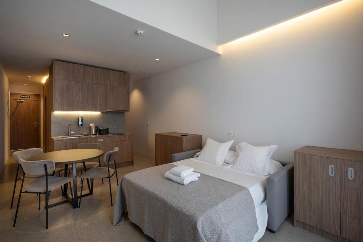 A modern hotel room with a bed, bedside tables, a desk, and a chair.