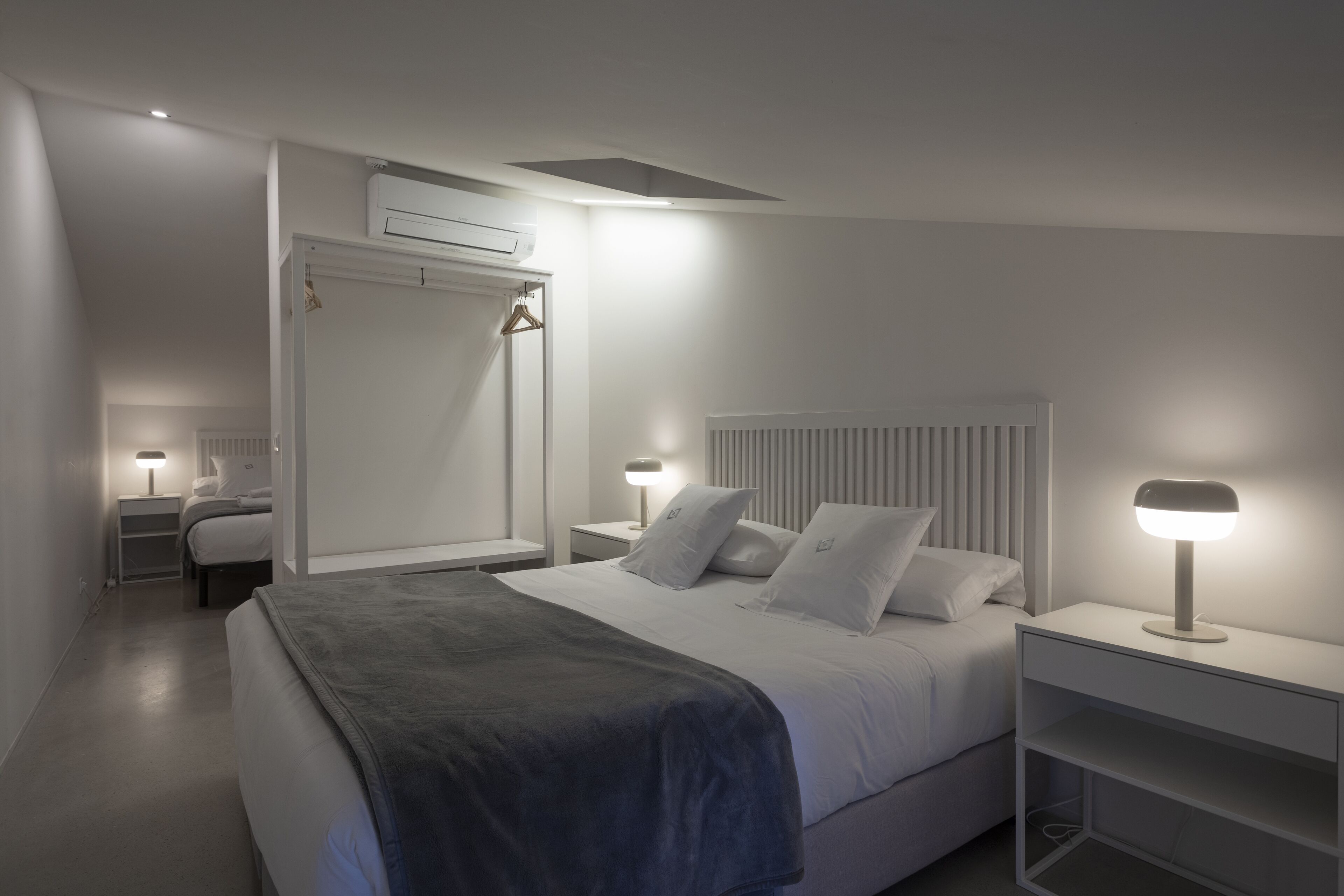 A modern bedroom with a bed, bedside tables, a wardrobe, and an air conditioning unit.