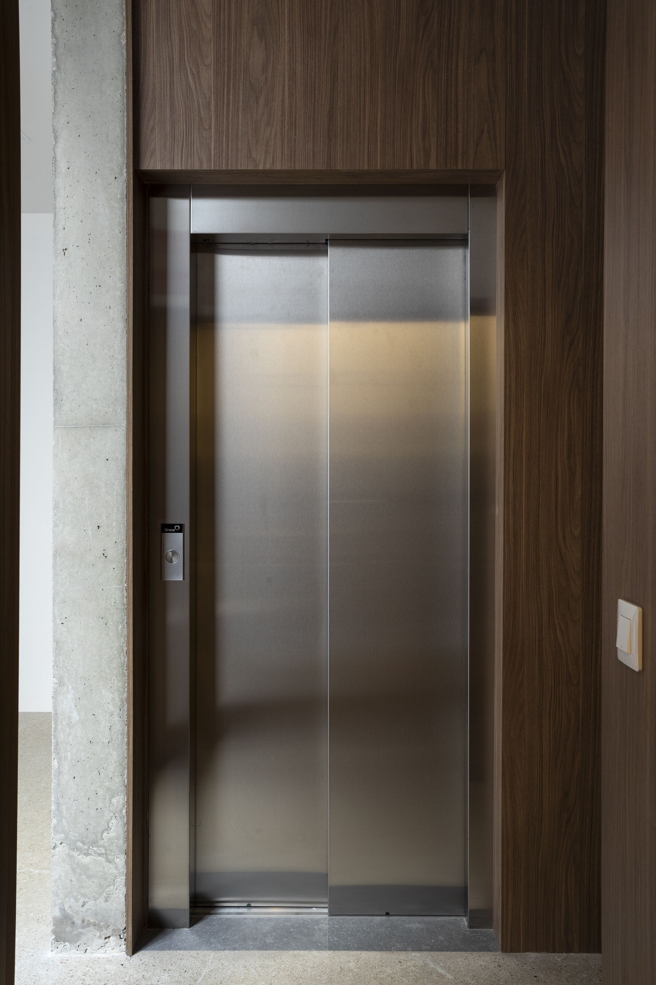 Un ascensor moderno con detalles metálicos, paneles de madera en las paredes y un panel de control sencillo.