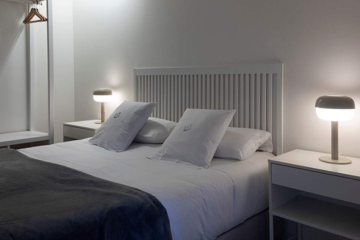A modern bedroom with a bed, two bedside tables, and two wall-mounted lamps.