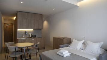 A modern hotel room with a bed, bedside table, and a small kitchenette.