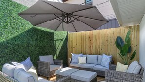 Un patio con mobiliario de mimbre, un paraguas grande y una valla de madera.
