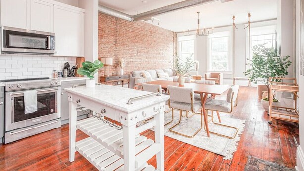 Une cuisine moderne avec des meubles blancs, un mur en briques et un coin repas comprenant une table et des chaises blanches.